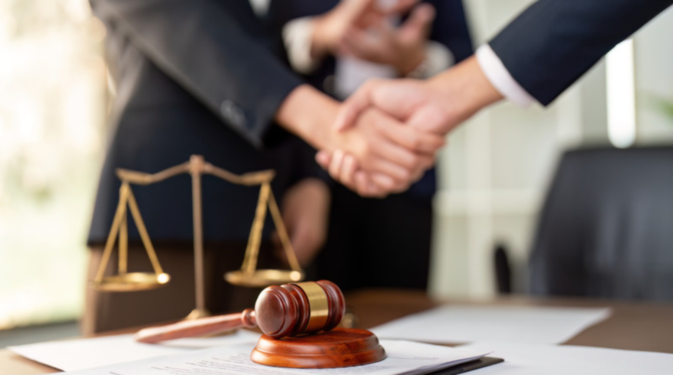 Two people in business attire shake hands near a desk with a gavel and scales of justice, suggesting a legal agreement or settlement with a Utah personal injury attorney in Midway.