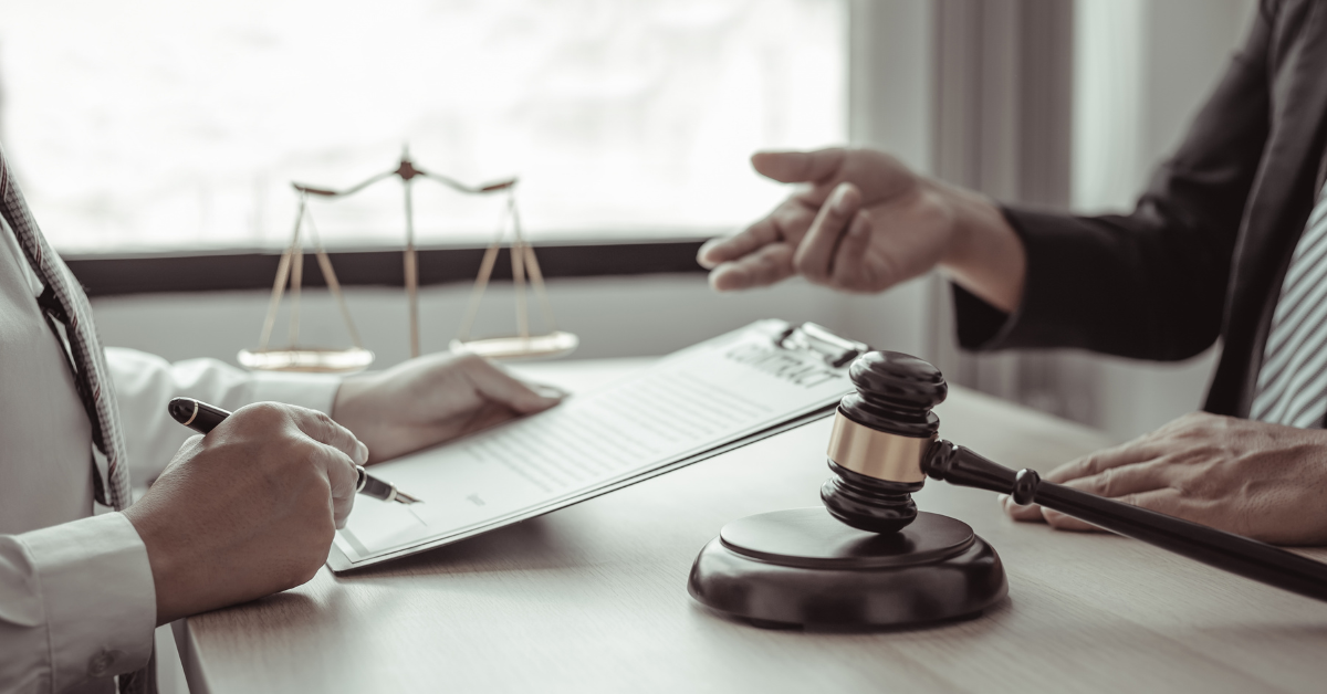 Two people in business attire sit at a desk with a gavel and legal scales, one writing on a document while the other gestures—a scene typical for a Utah truck accident lawyer in Park City.